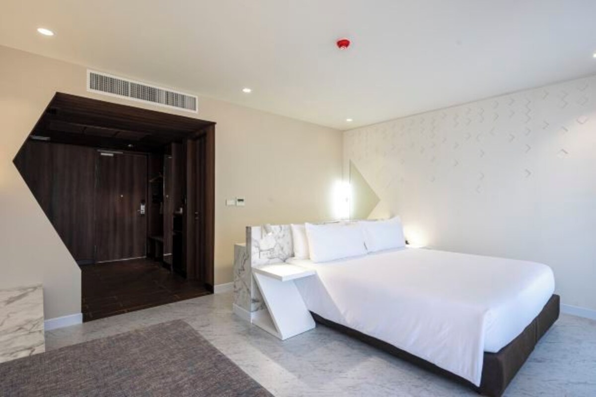 A modern bedroom with a large bed, a built-in nightstand, and a unique geometric wall design.