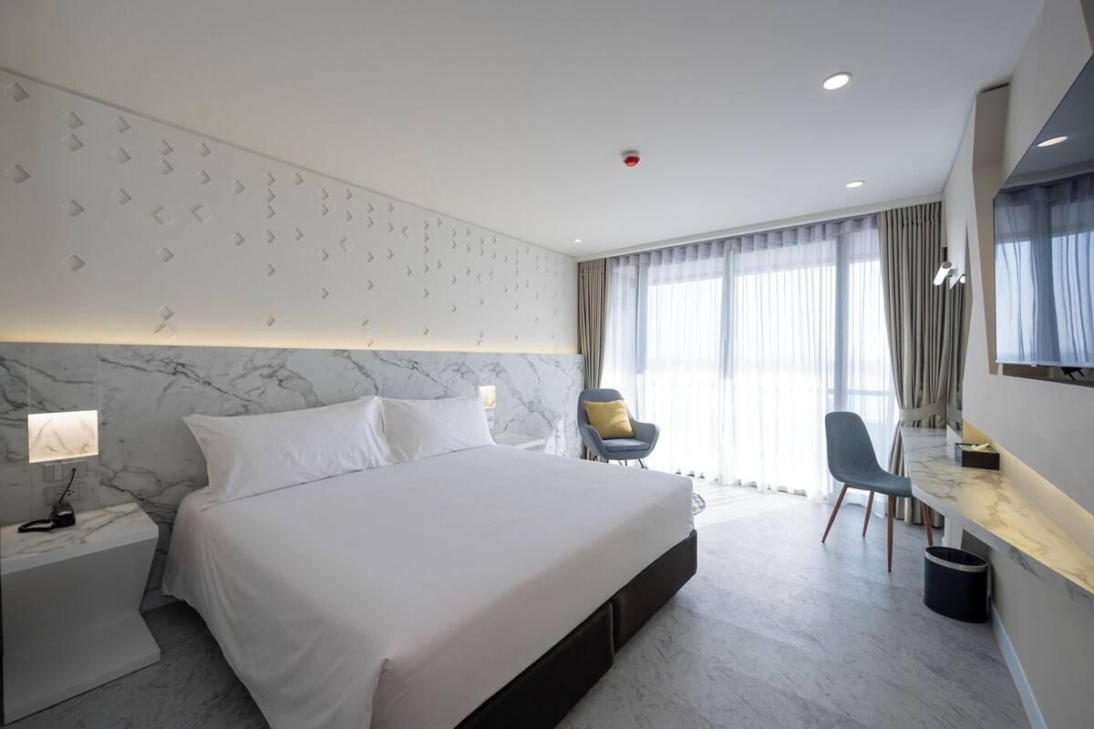Una habitación de hotel moderna con una cama grande, un escritorio, una silla y una pared con diseño de mármol.
