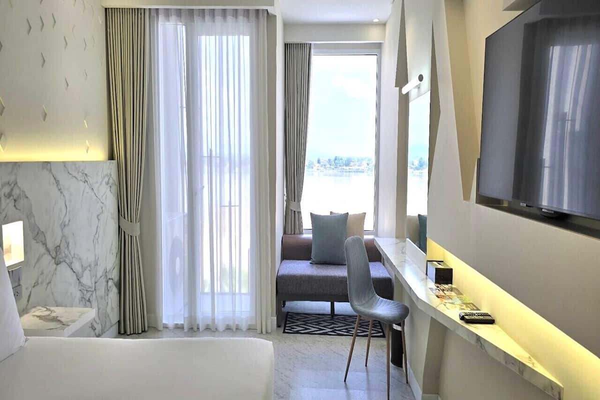 Habitación de hotel con cama, escritorio con silla, televisor y vista al exterior.