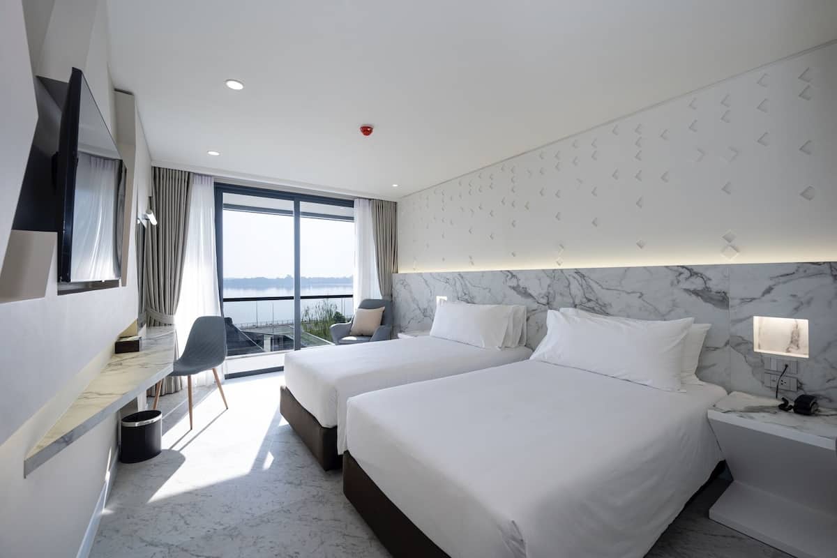 Habitación de hotel con dos camas, un escritorio, una silla y un ventanal con vistas.