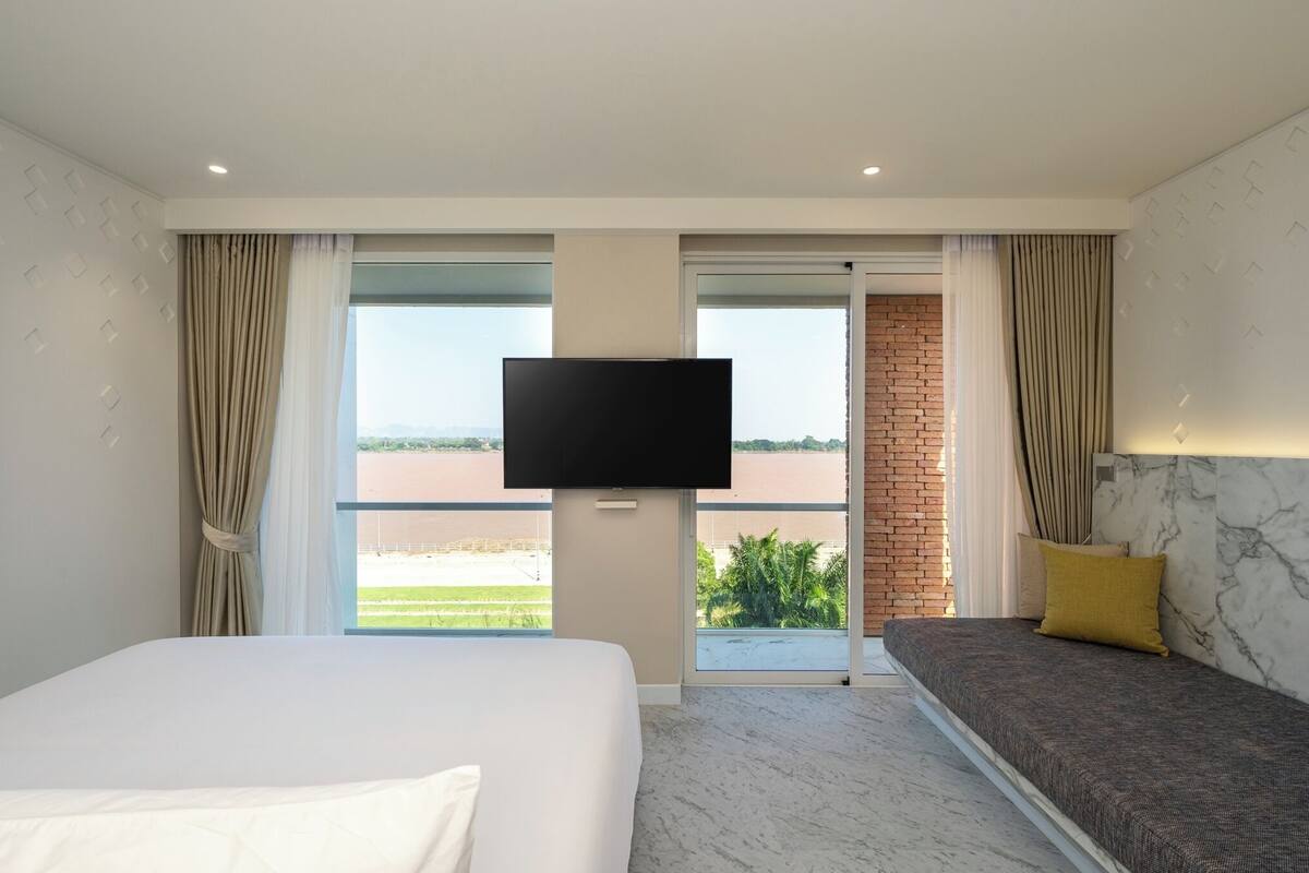 Habitación de hotel con cama, sofá, televisión y balcón con vistas a una masa de agua.