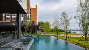 A modern hotel with a rooftop pool area, lounge chairs, and a view of a lake. - VELA Dhi Nakhon Phanom (Nakhon Phanom)