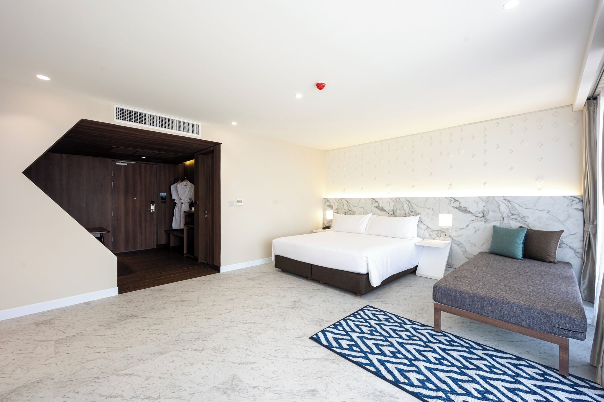 A modern hotel room with a large bed, a seating area, a wardrobe, and a bathroom.