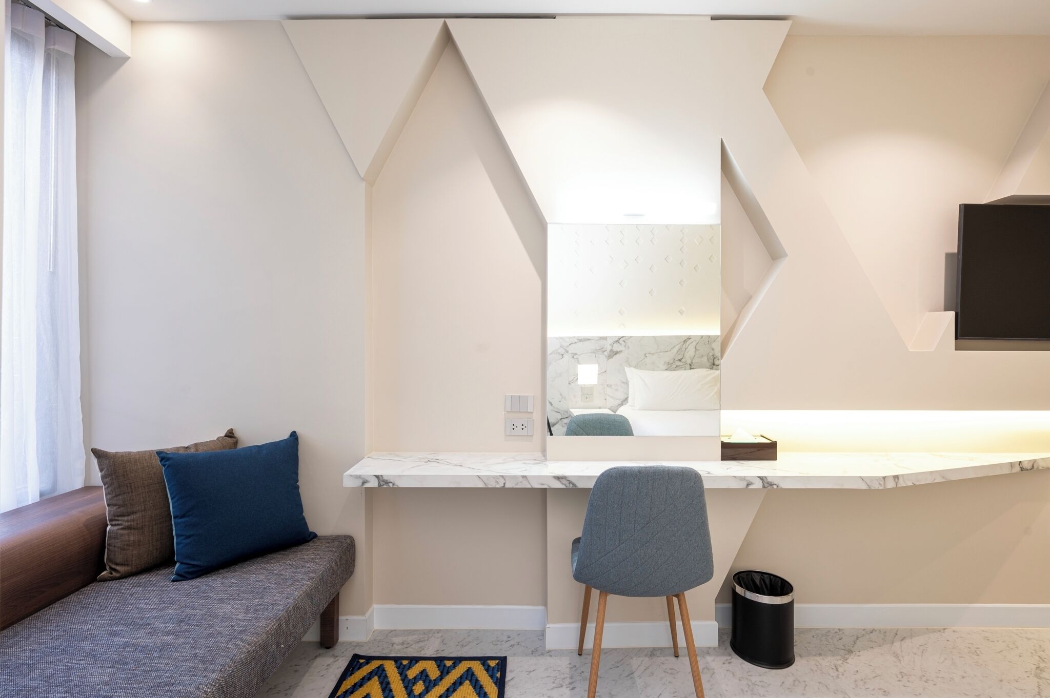 A modern room with a sofa, a desk with a chair, a mirror, and a TV.