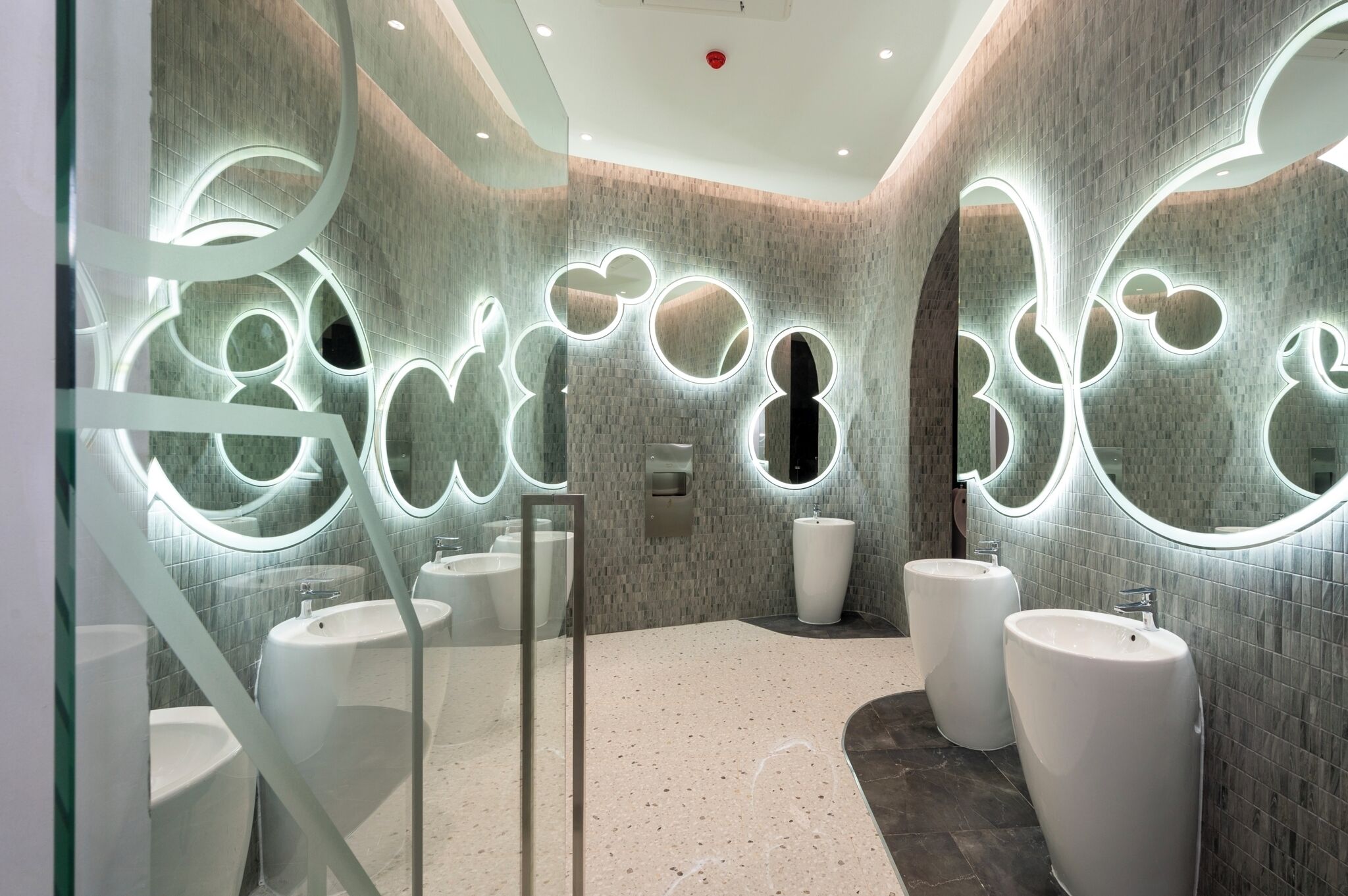 A modern bathroom with multiple sinks, a glass partition, and decorative lighting.