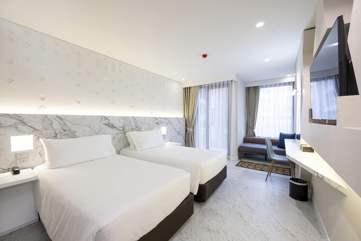 Habitación de hotel con dos camas, un escritorio, una silla, un televisor y una ventana con cortinas.