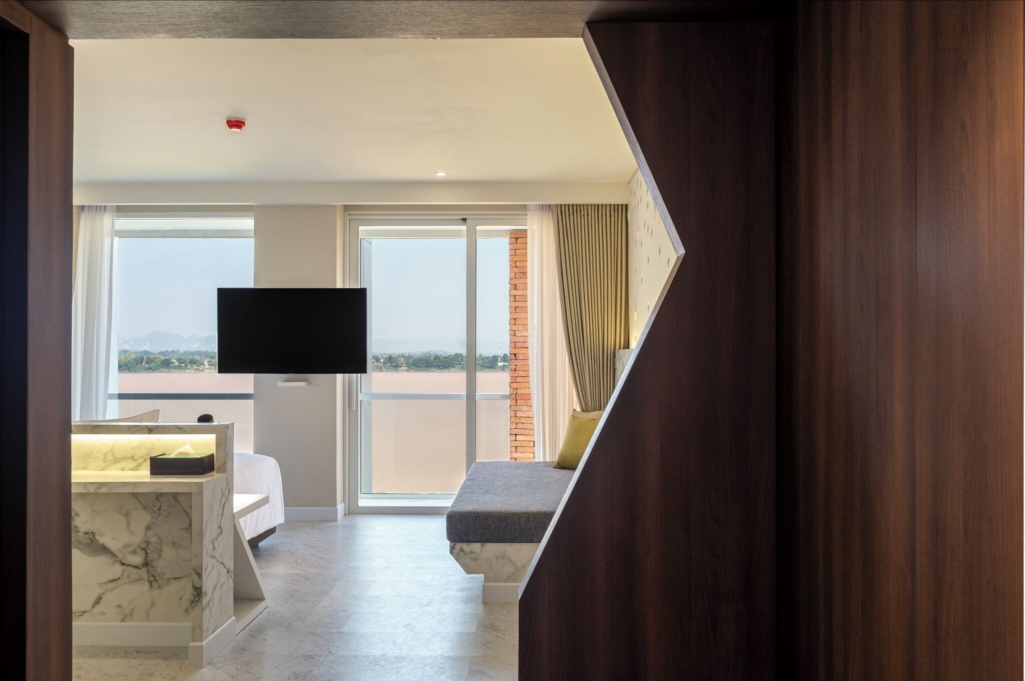Habitación de hotel con un ventanal grande, televisor de pantalla plana, escritorio de mármol y cama con vista a la playa.