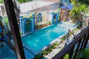 Une piscine avec un toboggan, entourée de verdure et délimitée par une clôture bleue.