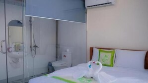 A hotel room with a wooden bed, a glass-enclosed shower, an air conditioning unit, and a green pillow. - 86 Homestay Phan Thiet (Phu Thuy)