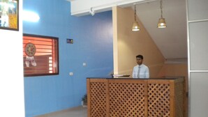 A reception area with a blue wall, a wooden reception desk, and a ceiling fan. - Rains Inn Eco Hotel (Diphu)