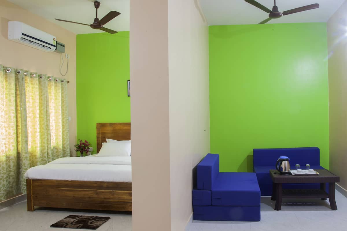 Quarto com cama, sofá azul, mesa pequena com chaleira e ventilador de teto.