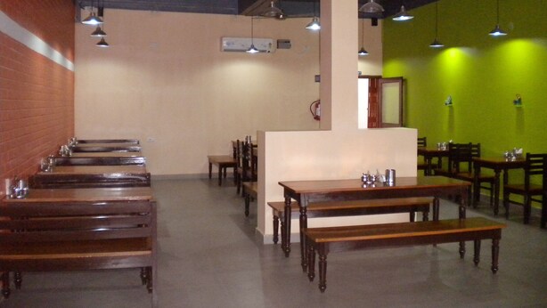 A restaurant interior with wooden tables and benches, a brick wall on one side, and a green wall on the other. - Rains Inn Eco Hotel (Diphu)