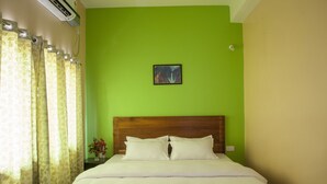 A neatly made bed with white linens, a wooden headboard, and a green wall with a framed picture above it. - Rains Inn Eco Hotel (Diphu)