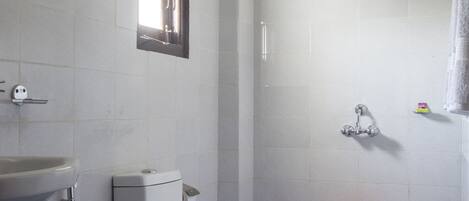 Un baño con inodoro, lavamanos, ducha y un cubo rojo en el suelo.