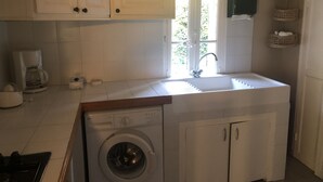 A compact kitchen with white cabinets, a built-in washing machine, a coffee maker, and a window with a view of greenery. - Lovely, sunny, very quiet apartment facing south in Sanary sur mer  (Sanary-sur-Mer)