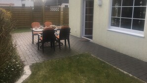 Une terrasse avec une table et des chaises, une clôture en bois et une maison avec une fenêtre.