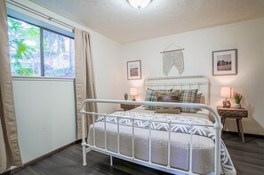 A bedroom with a metal bed frame, a bedside table with a lamp, and a window with curtains.