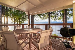 Un patio techado al aire libre con una mesa redonda y sillas, una parrilla y vistas al agua.