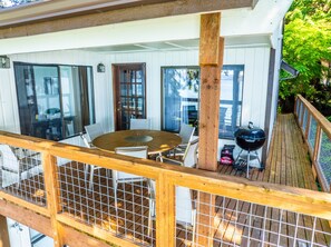 A deck with a round table and chairs, a grill, and a view of the surrounding area.