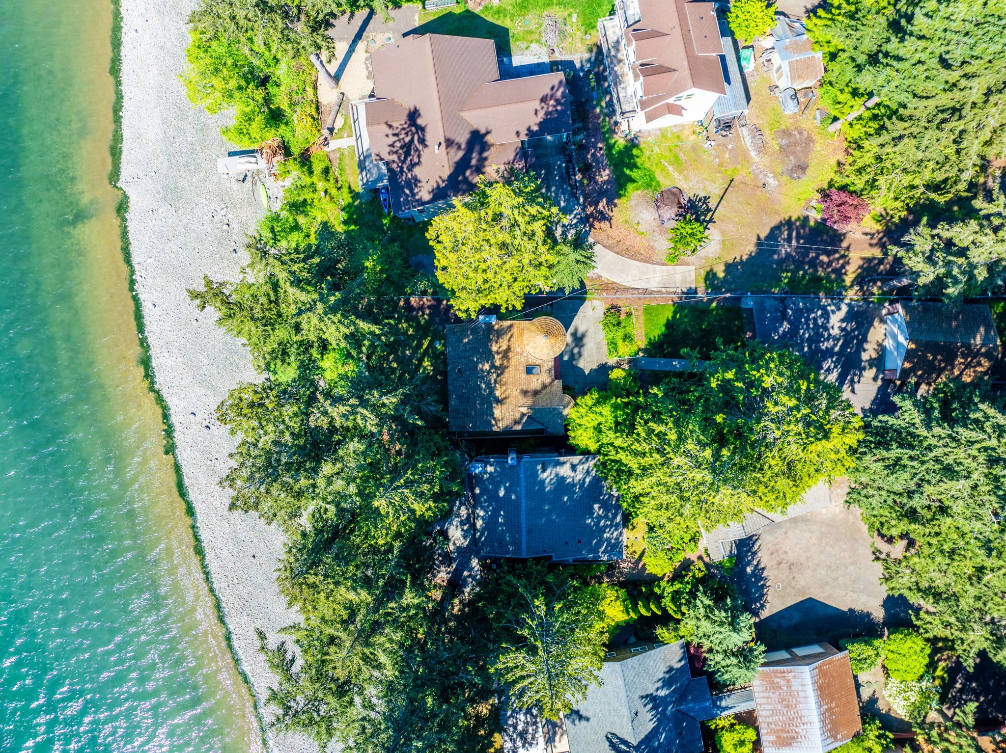 Vue aérienne d’une propriété située sur la côte, comprenant plusieurs bâtiments, une plage et une végétation luxuriante.