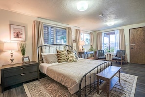 A bedroom with a bed, bedside tables, a desk, chairs, and a view of the outdoors. - Fairyland Cottage: Waterfront+Hot Tub+Beach+Clam (Poulsbo)