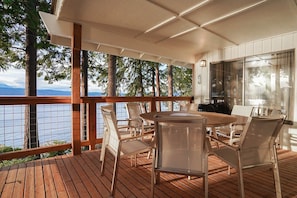 An outdoor deck with a round table and chairs, overlooking a body of water and trees. - Fairyland Cottage: Waterfront+Hot Tub+Beach+Clam (Poulsbo)
