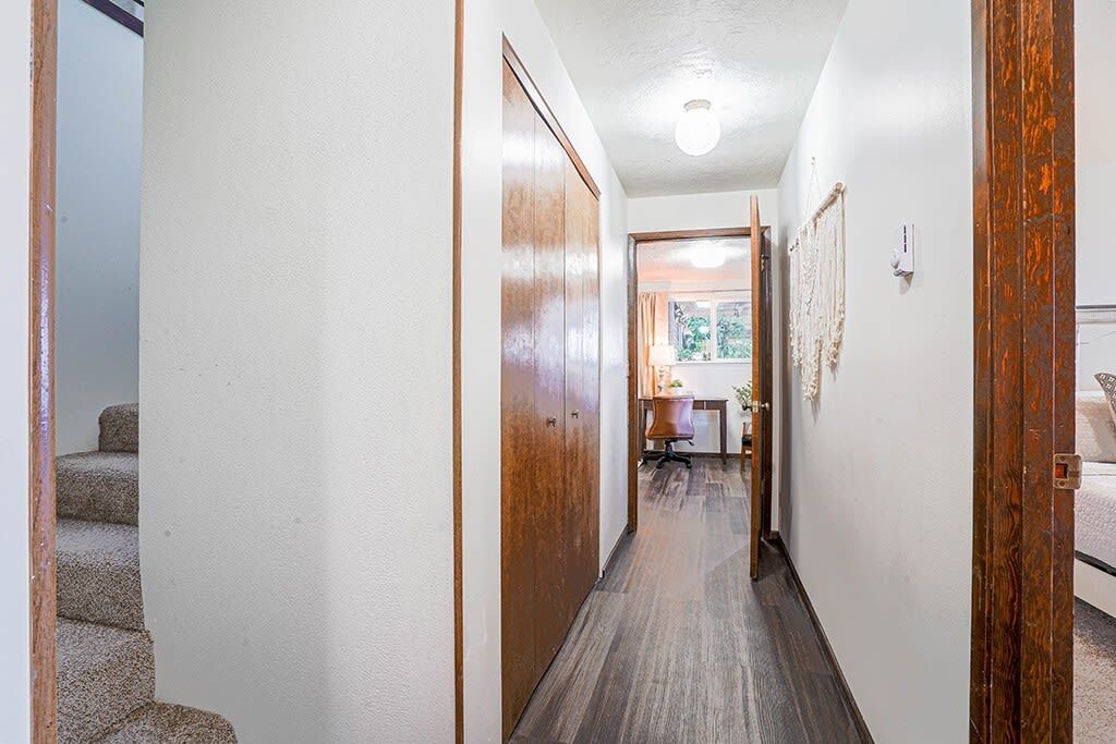 Un couloir avec une porte en bois, un escalier et un bureau avec une chaise.