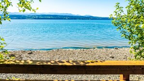 A lakeside view with a rocky shore and a wooden bench. - Fairyland Cottage: Waterfront+Hot Tub+Beach+Clam (Poulsbo)