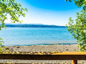 A lakeside view with a rocky shore and a wooden bench. - Fairyland Cottage: Waterfront+Hot Tub+Beach+Clam (Poulsbo)