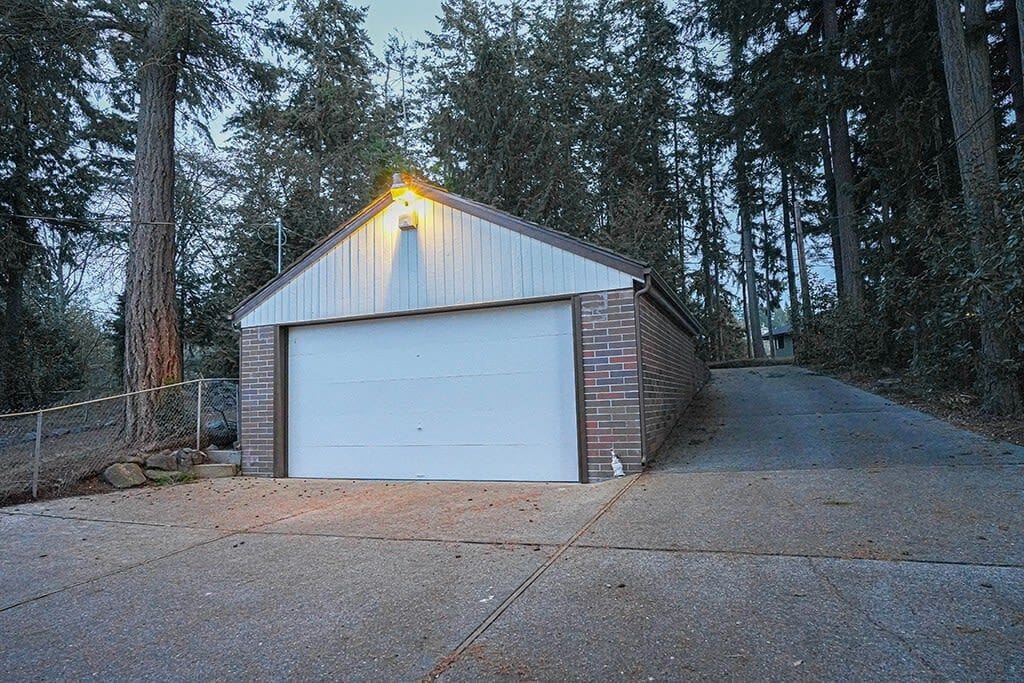 Un bâtiment d’un seul étage, doté d’une porte de garage, entouré de grands arbres.