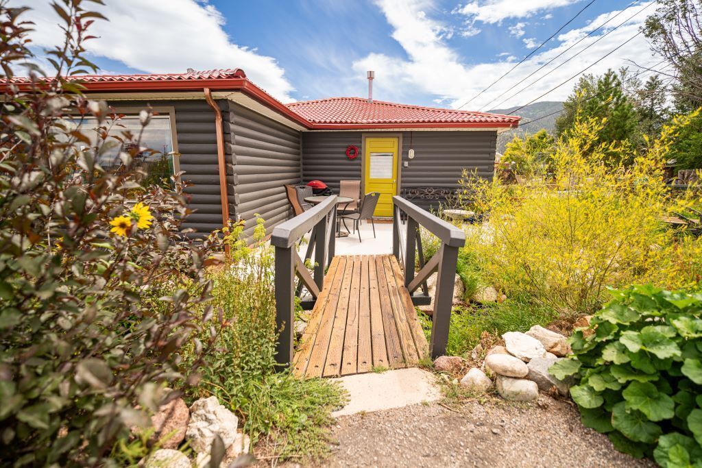 A log cabin with a red roof, a wooden deck leading to the entrance, and a yellow door.