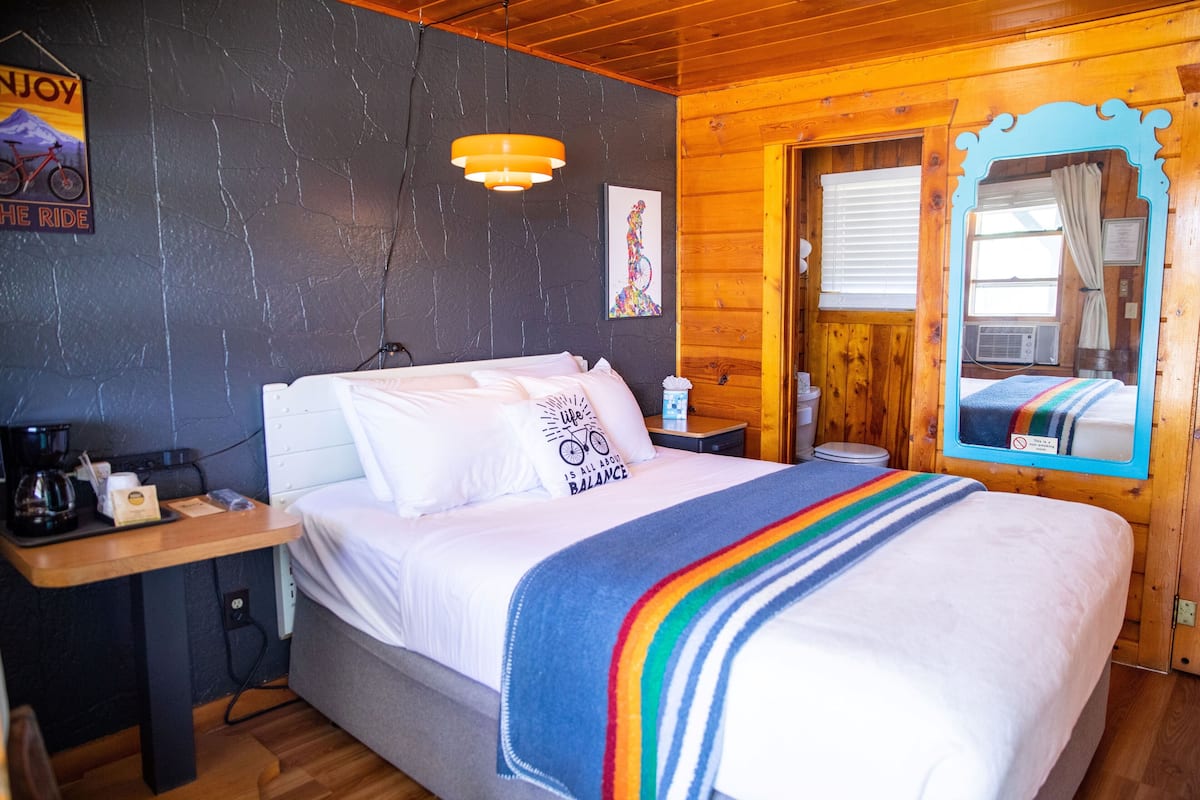 A cozy room with a bed, a wooden desk, a mirror, and a wall with a poster.