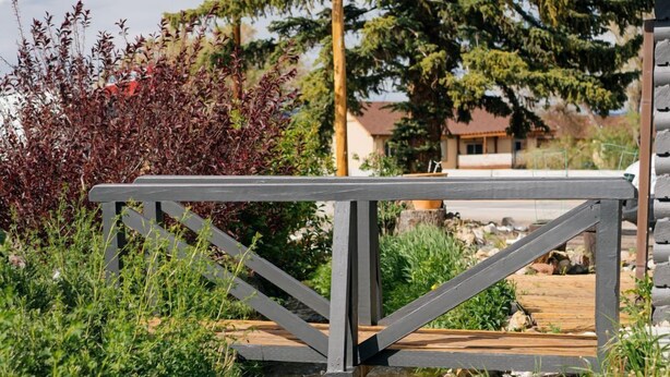 Een houten brug over een beekje, met een metalen leuning, omringd door groen en bomen.