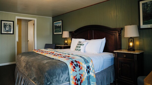 A hotel room with a large bed, two bedside lamps, a door, and framed pictures on the walls. - The Lodge at Poncha Springs (Salida)