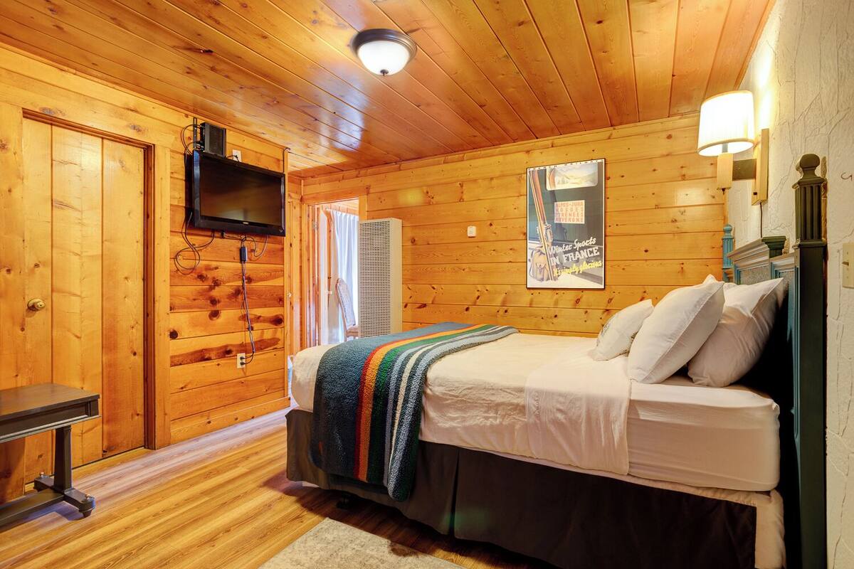 A cozy log cabin bedroom with a bed, a television, a heater, and a poster on the wall.