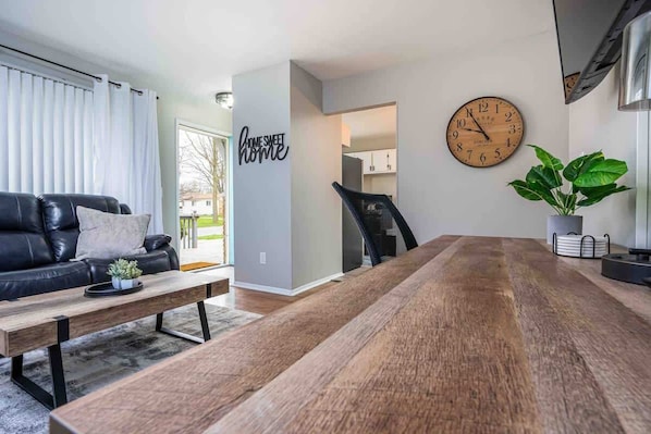 Una sala de estar moderna con una mesa de comedor de madera, un sofá de cuero negro, un reloj y una planta en maceta.