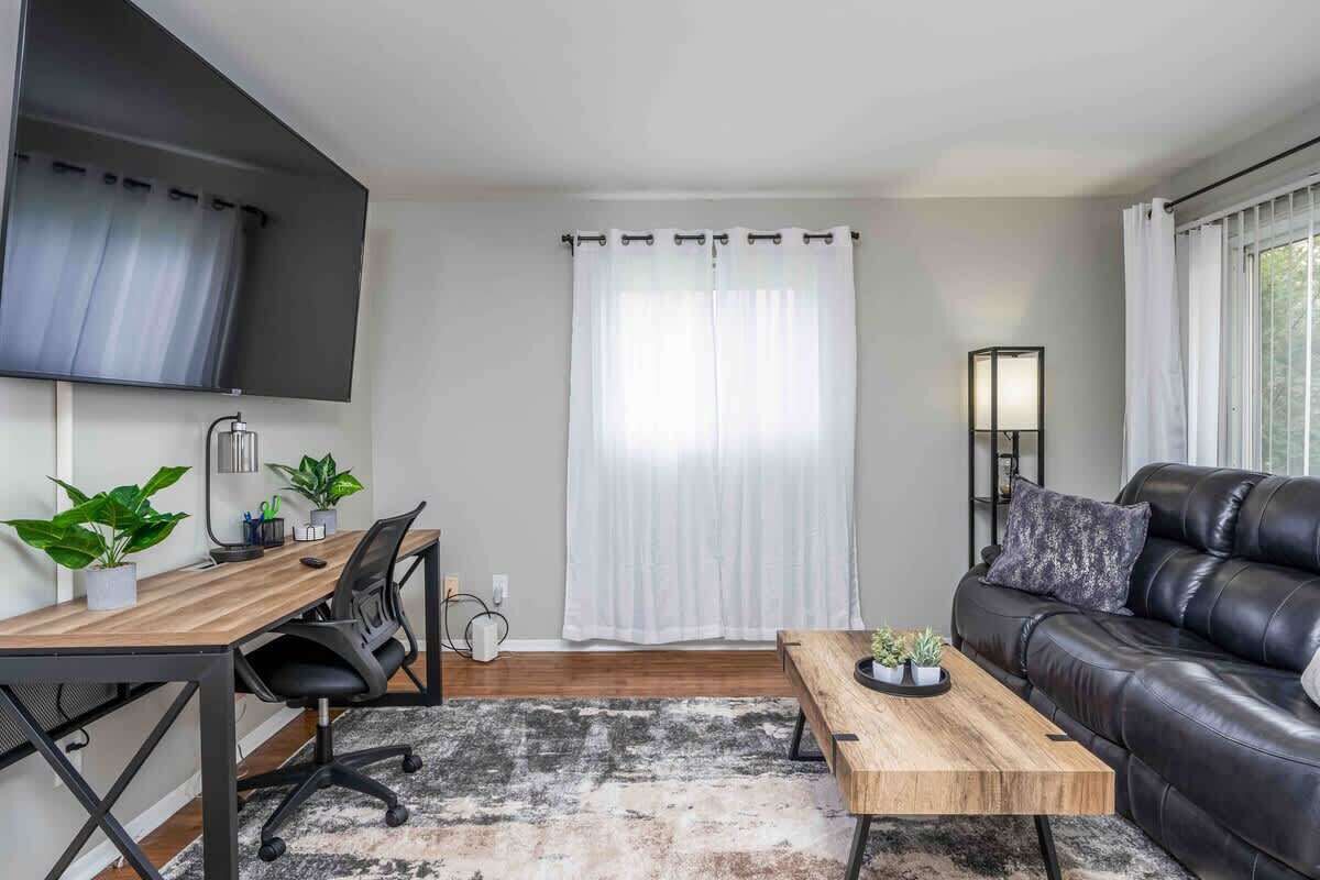Ein modernes Wohnzimmer mit einem Holztisch, einer schwarzen Ledersofa und einem großen Fenster mit weißen Vorhängen.