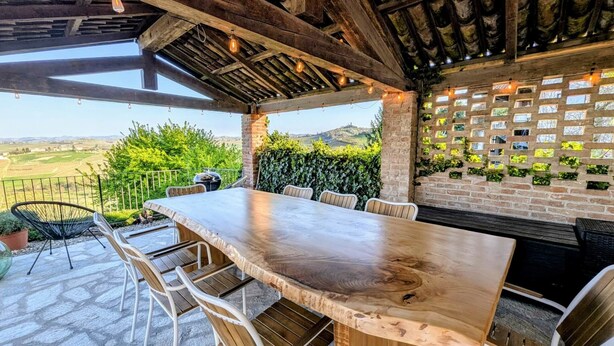 Eine Terrassenanlage im Freien mit Holztisch und -stühlen, einer Ziegelwand mit Pflanzen und Blick ins Grüne.