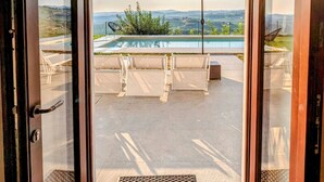 Eine Glastür führt zu einer Außenpatio mit Pool, Liegestühlen und Sonnenschirm.