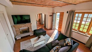 Ein Wohnzimmer mit Kamin, einer Couch, einem Fernseher und Blick ins Freie.