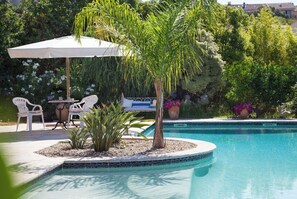 A poolside area with a table and chairs, a palm tree, and a white umbrella. - Modern villa with swimming pool and private garden, (Bormes-les-Mimosas)