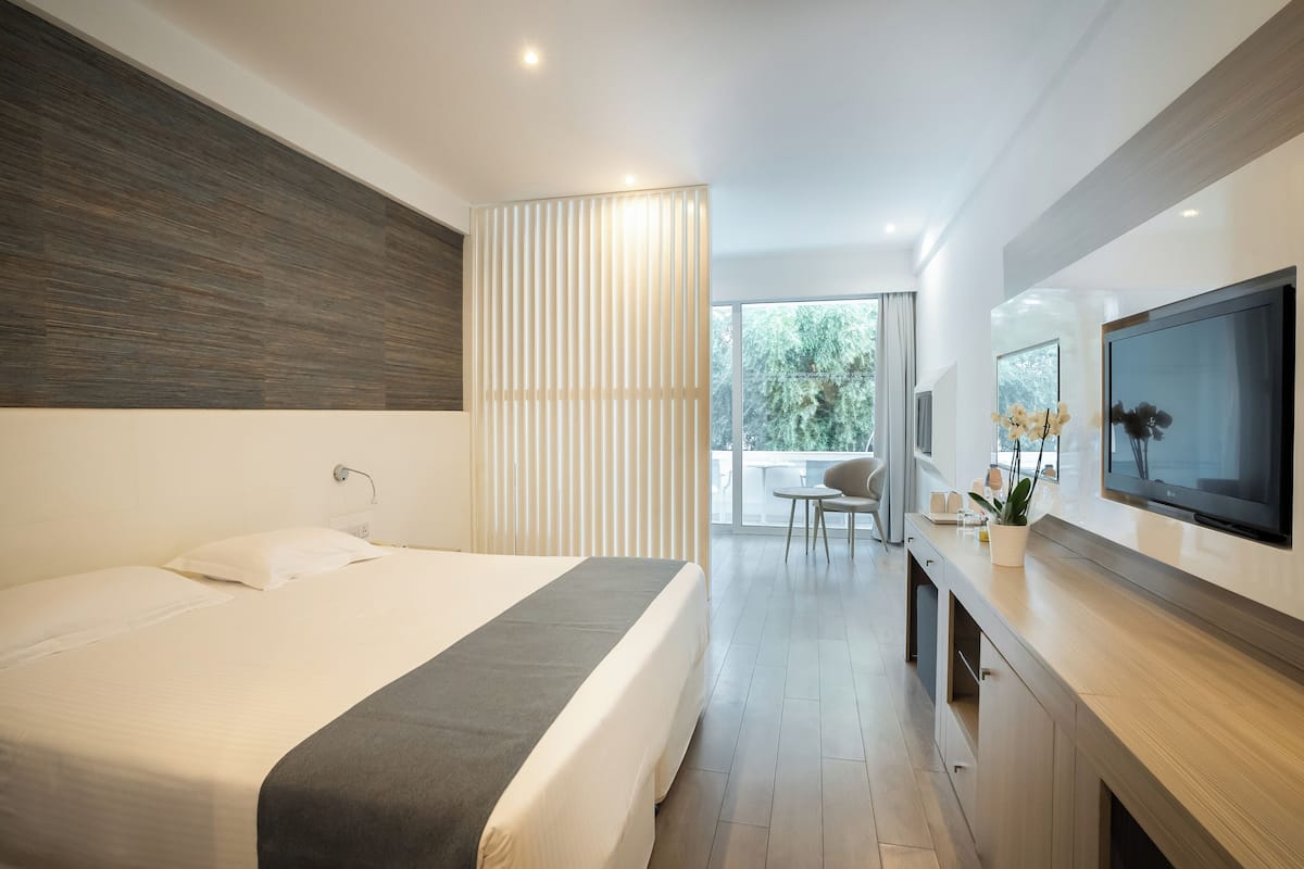 A modern hotel room with a large bed, a TV mounted on the wall, and a view of the outdoors through a large window.