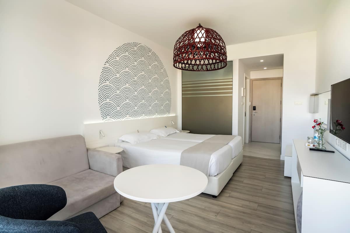 A modern hotel room with a large bed, a sofa, a small round table, and a TV.
