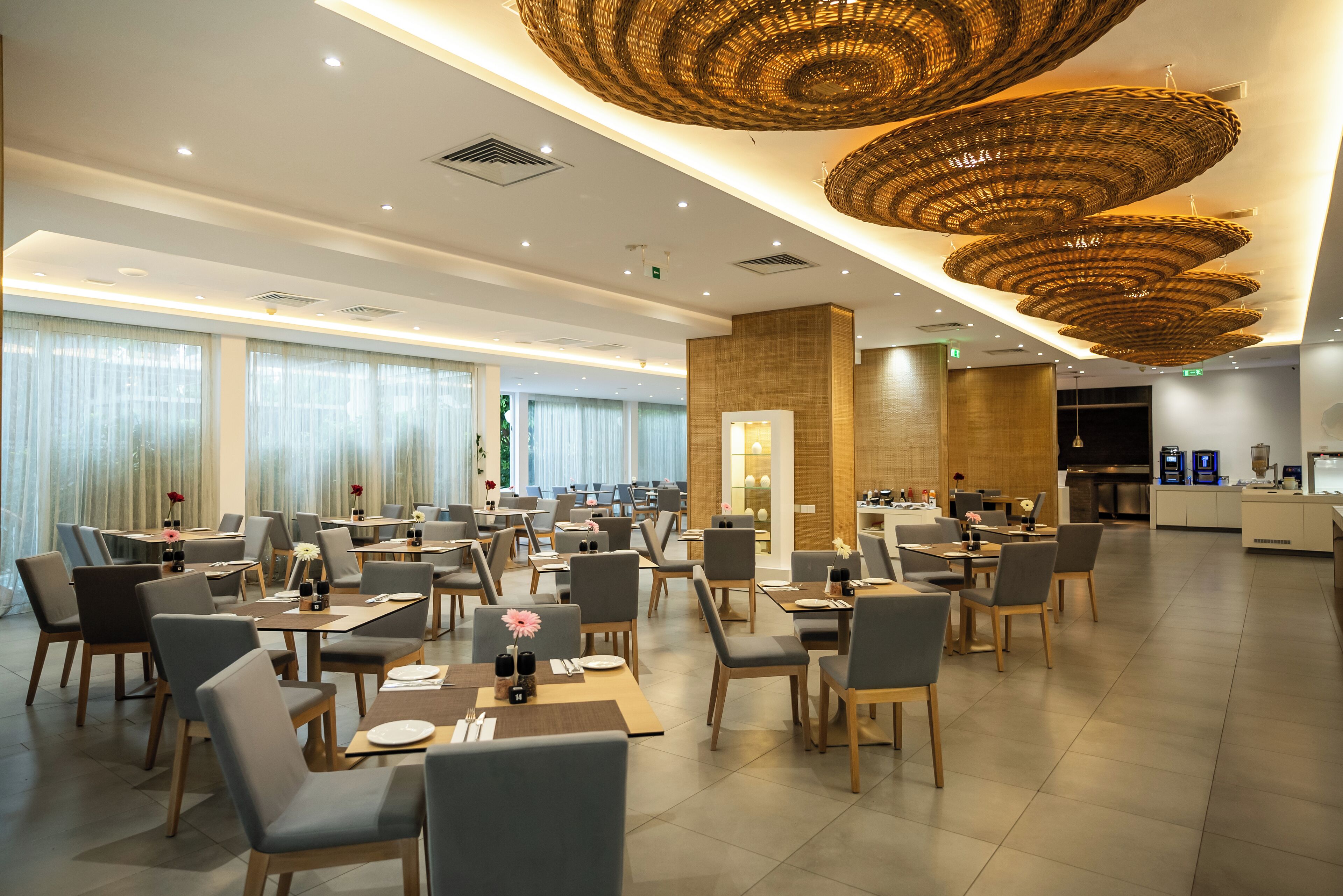 Un grand espace dédié à la salle à manger, avec plusieurs tables et chaises, un pilier central et une cuisine en arrière-plan.