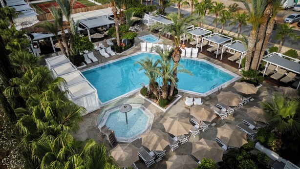 An aerial view of a resort with a central swimming pool, lounge areas, and palm trees. - MARGADINA HOTEL (Ayia Napa)