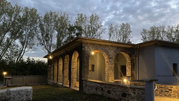 Un bâtiment en pierre doté de fenêtres en arc de cercle et d’une façade en pierre, comprenant un petit espace extérieur aménagé avec une table et des chaises.