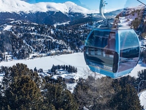 Un teleférico con la inscripción "TURRACHER BOHEMIA", suspendido sobre un paisaje nevado con edificios y árboles abajo.