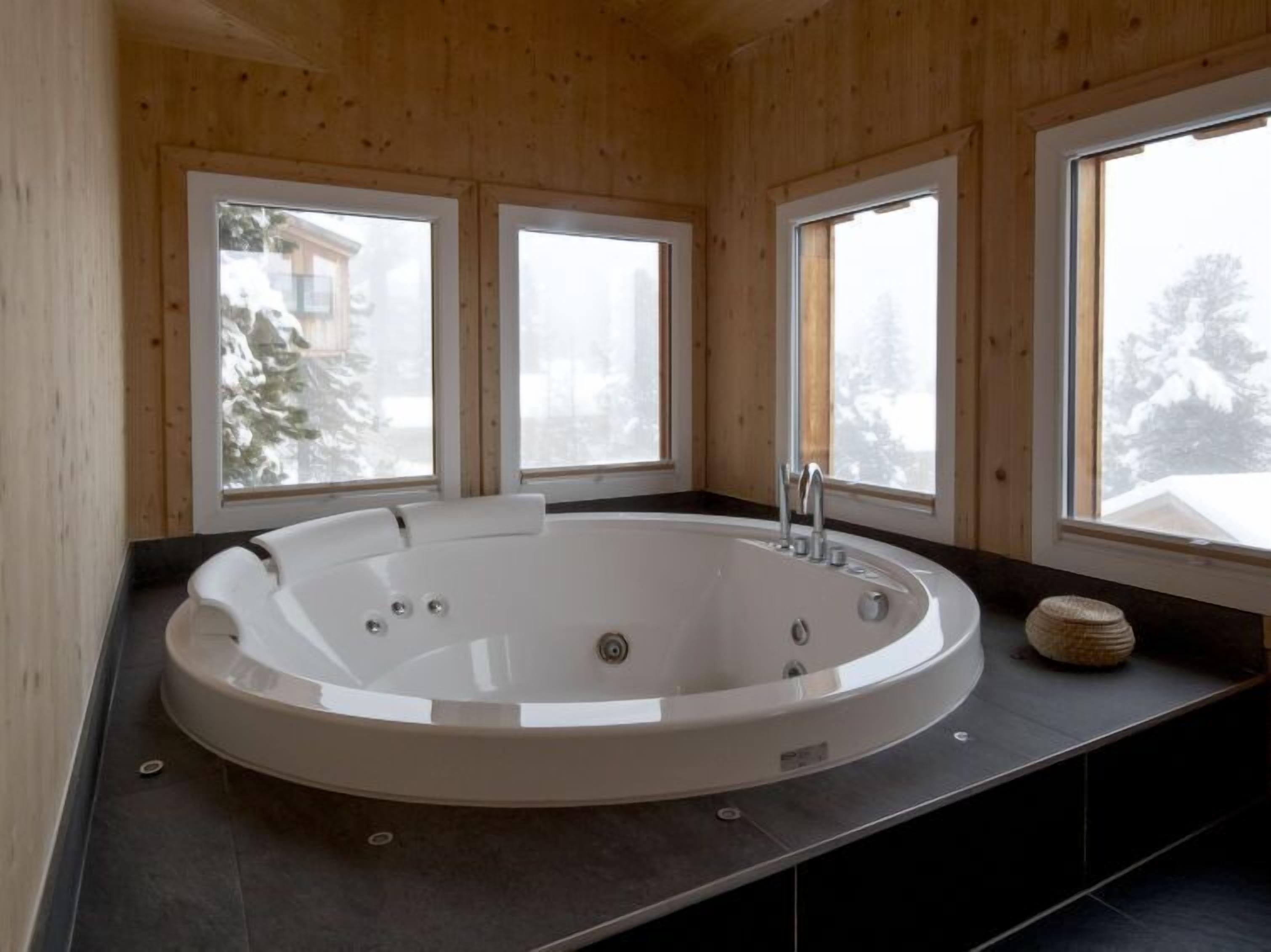 A modern bathroom with a freestanding bathtub, wooden walls, and large windows offering views of a snowy landscape.
