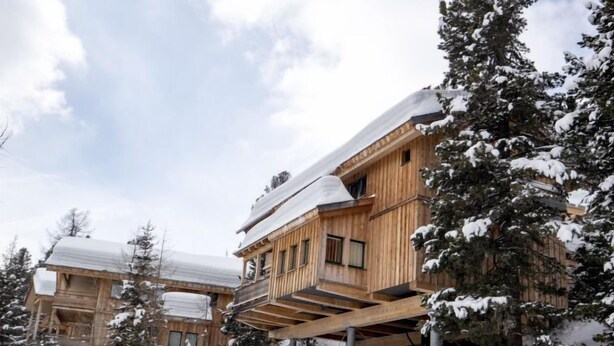 Una cabaña de madera con balcón, rodeada de árboles cubiertos de nieve.
