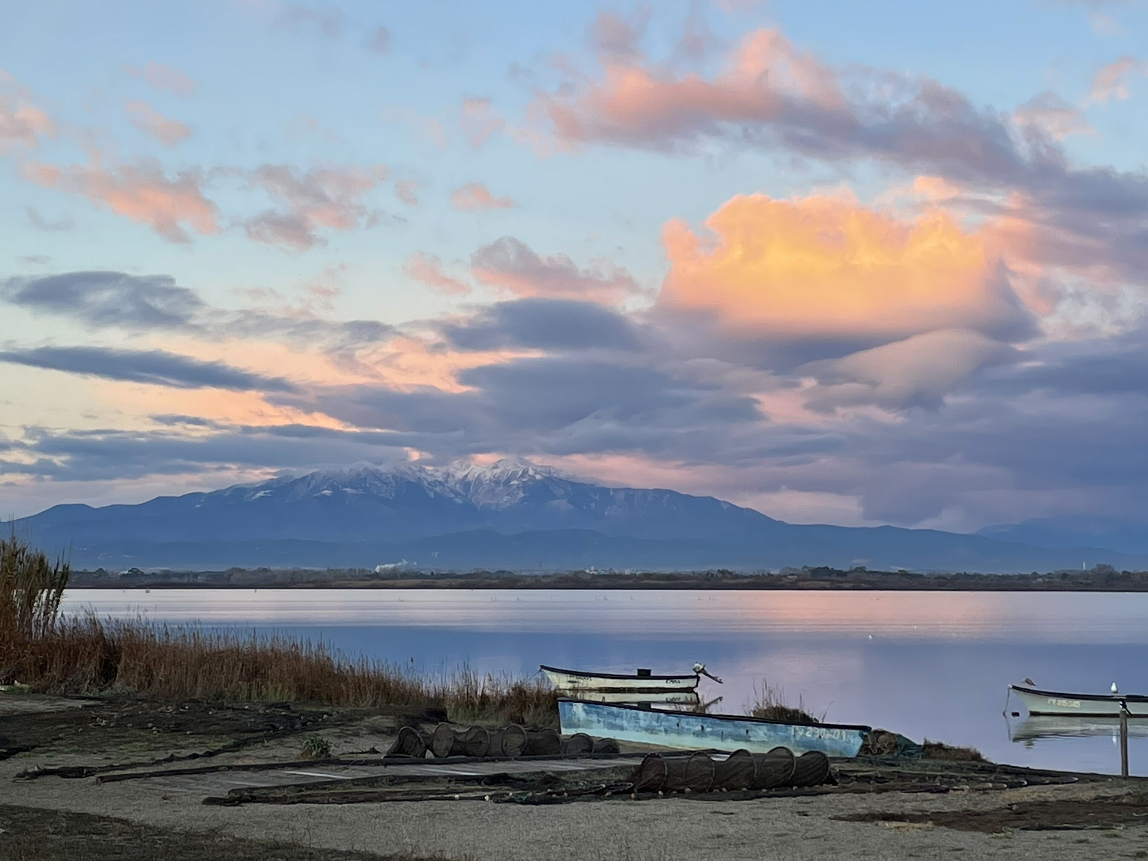 A lakeside view with boats, a clear sky, and mountains in the distance.